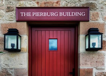 A photograph showing an exterior view, including the red entrance door, of the Pierburg Education Centre in Dumfries.
